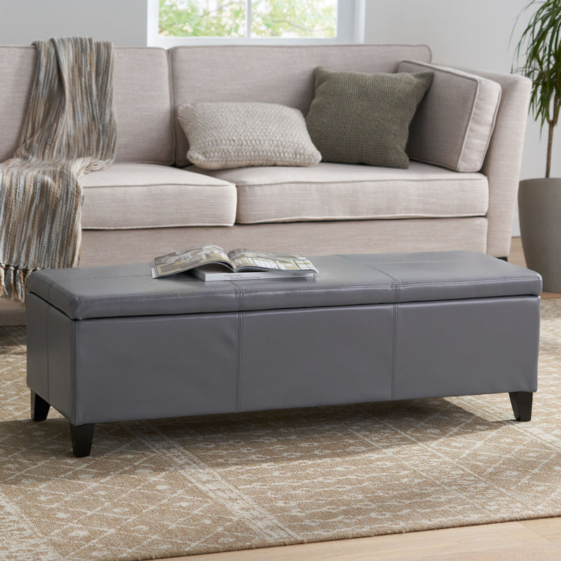 Dark gray upholstered storage ottoman with padded lid and low profile legs