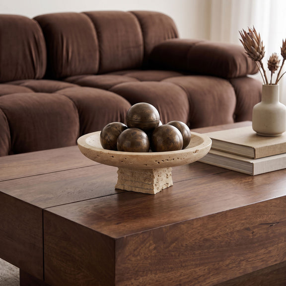 Travertine bowl with round rim and pedestal base, holding decorative spheres