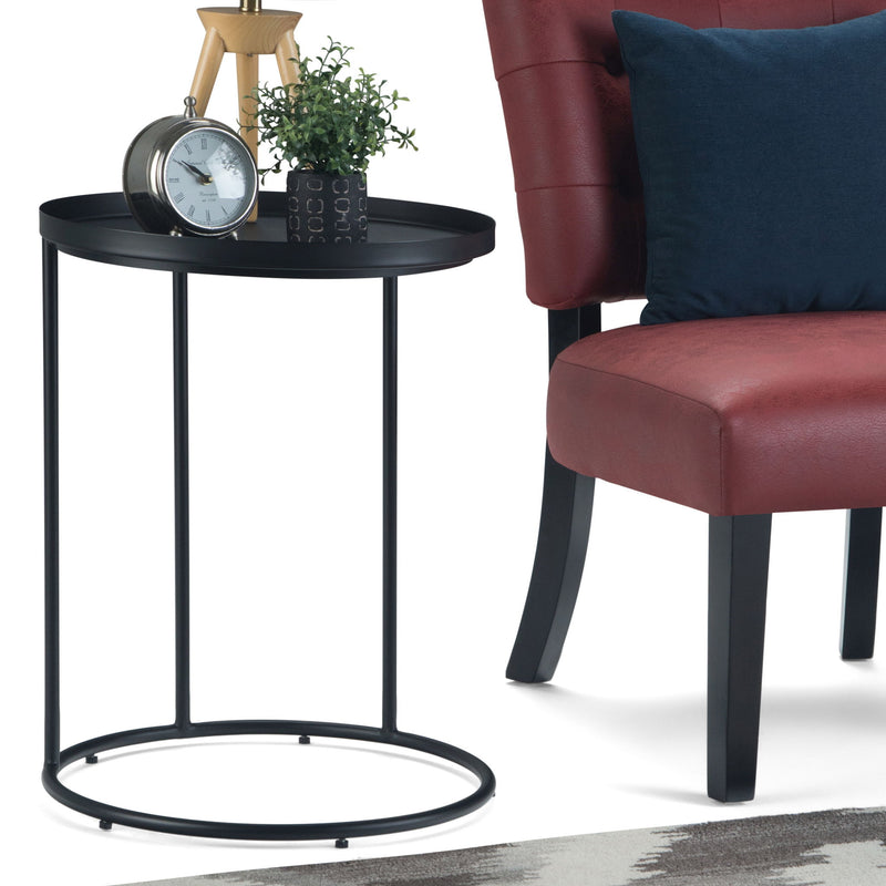 Black round metal side table with tray top and circular ring base, beside chair.