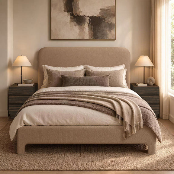 Light brown upholstered bed with pillows, quilt, and throw blanket on slat base