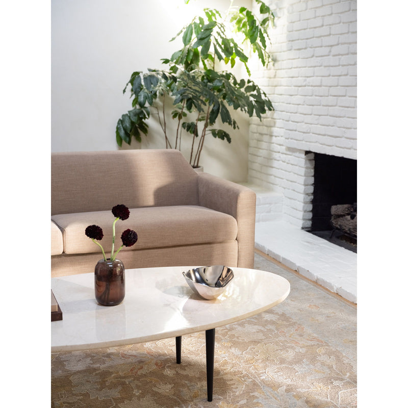 Round beige stone coffee table with dark tapered legs, vase and metal bowl on top