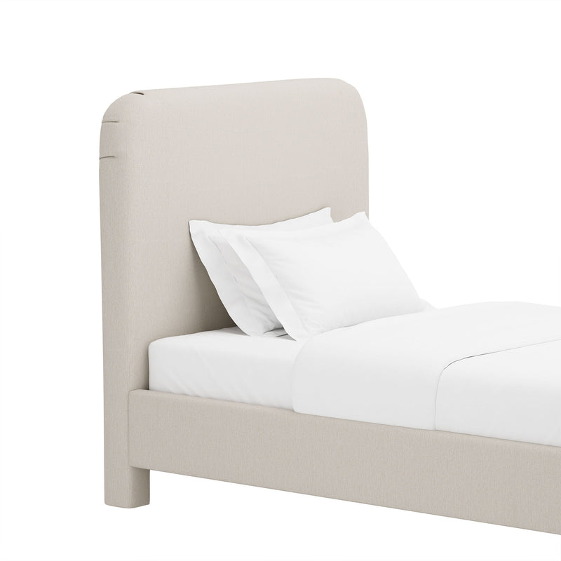 Light beige upholstered bed with rounded headboard and white pillows and bedding