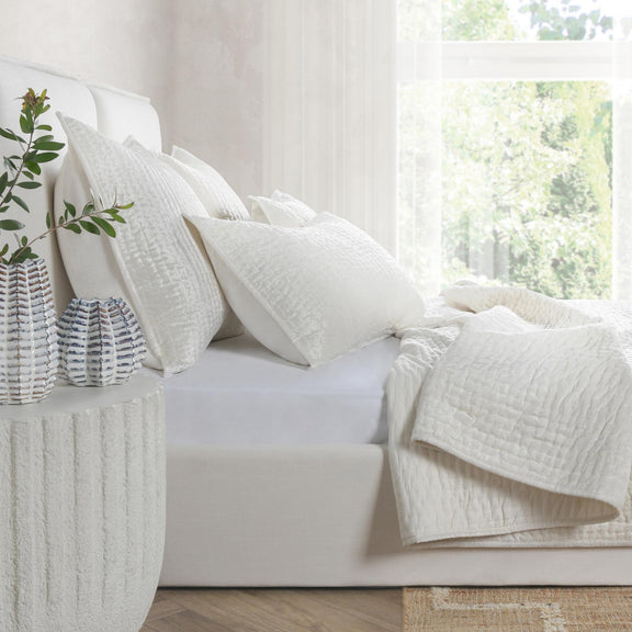 White velvet quilt set on a sofa with layered quilts and square pillow shams.