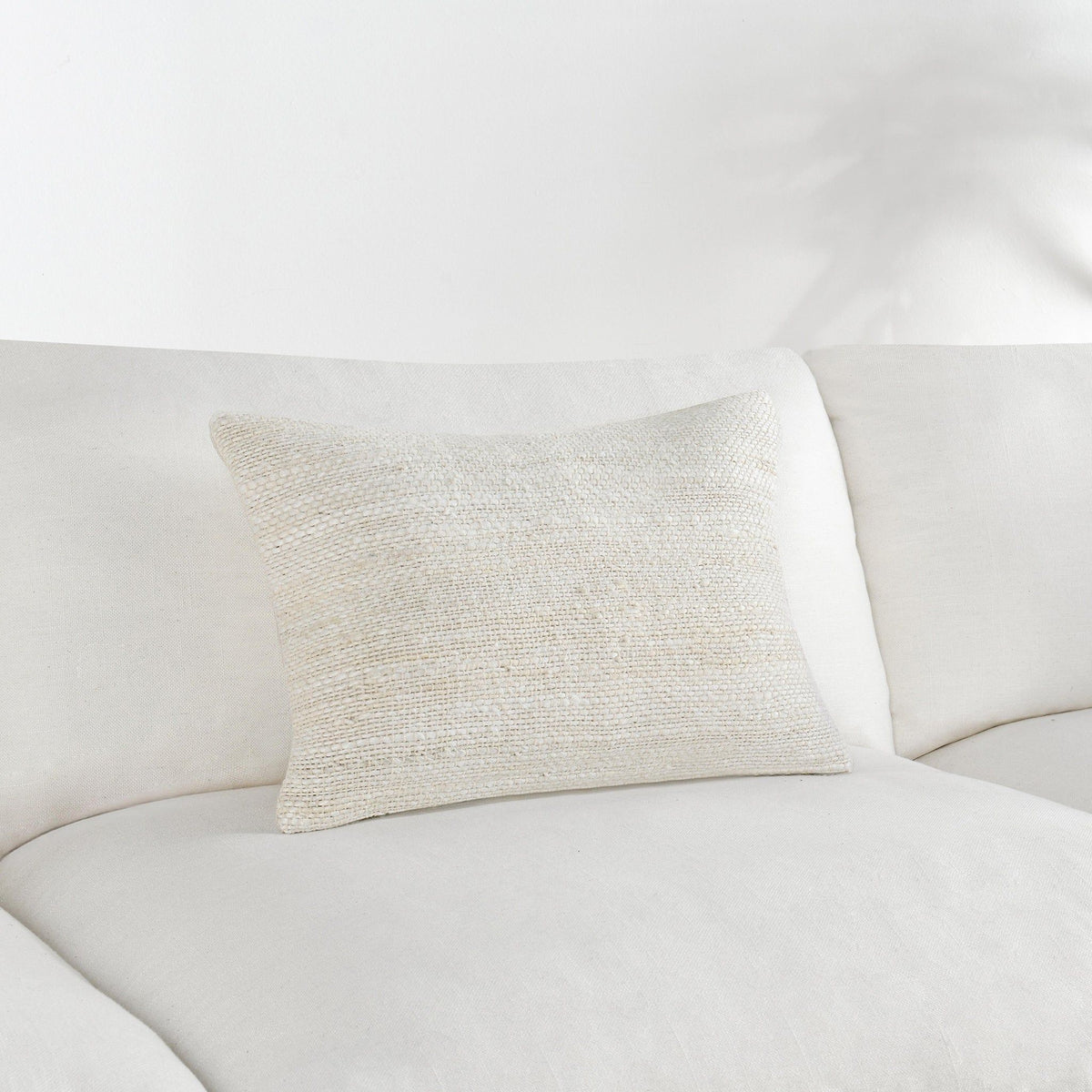 Ivory woven throw pillow on white sofa, square-rectangular shape.