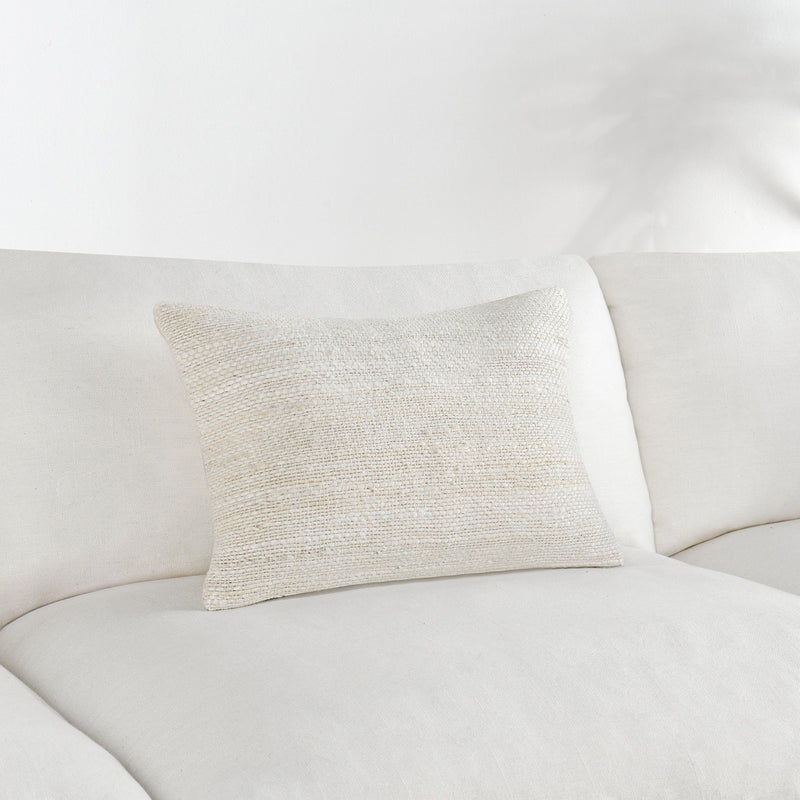 Ivory woven throw pillow on white sofa, square-rectangular shape.