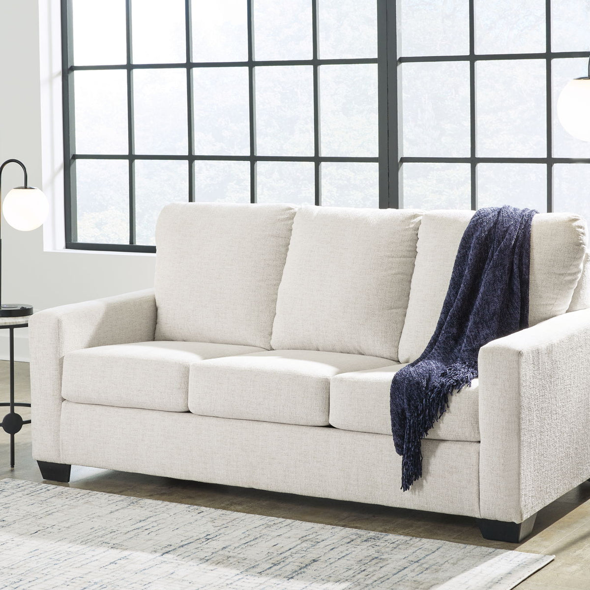Beige fabric sofa with three seat cushions and folded throw on right arm