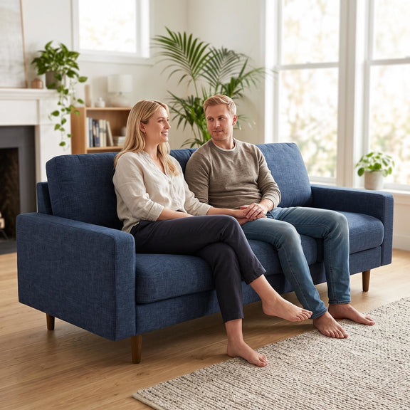 Dark blue three-seat fabric sofa with broad arms and loose back cushions, shown with two seated people.