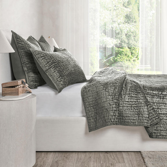 Gray velvet quilt set on a white sofa, featuring a textured quilt and pillow shams.