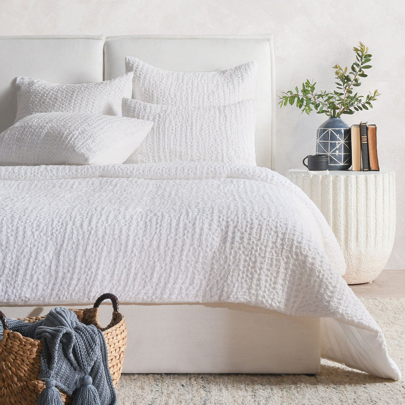 Ivory quilt with textured raised pattern, shown folded over a bed.