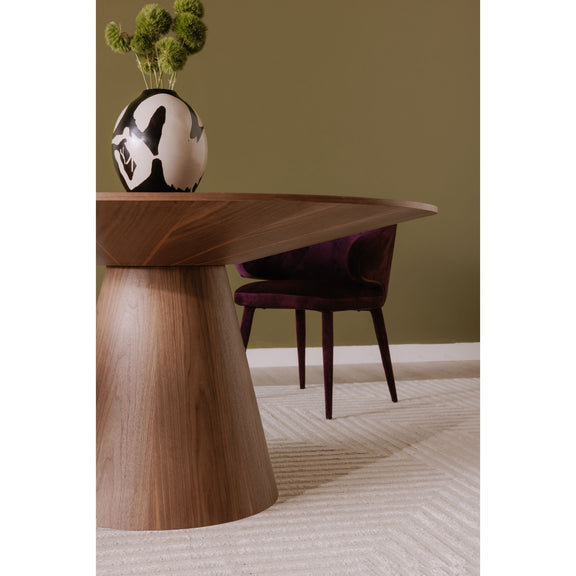 Round walnut dining table with central pedestal base beside upholstered chairs