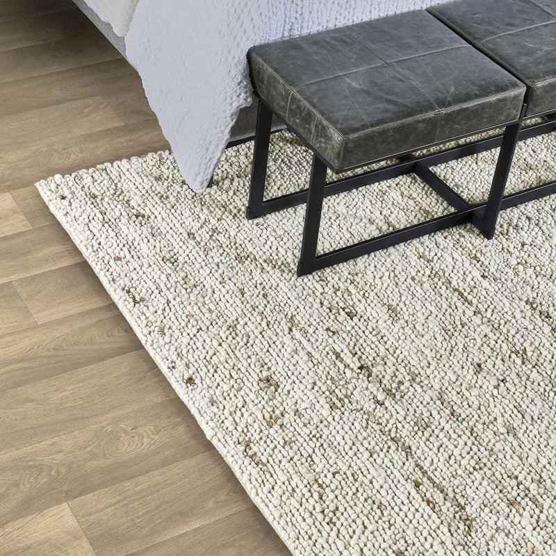 Natural wool rug with speckled texture beneath bench legs on wood flooring.