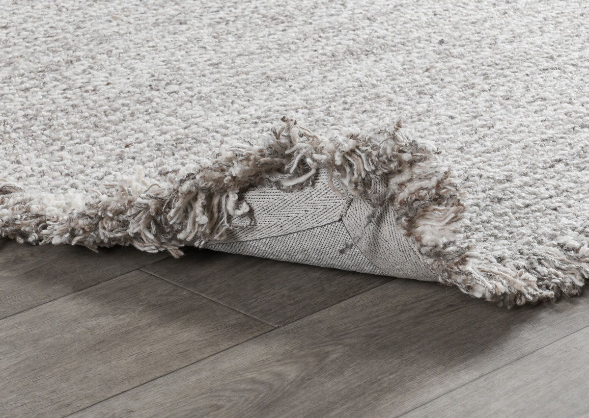 Wool rug detail: frayed fringe edge and backing visible along the side.