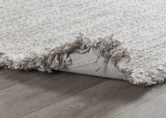 Wool rug detail: frayed fringe edge and backing visible along the side.