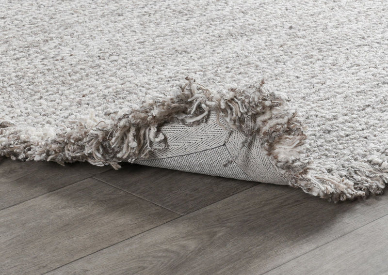 Wool rug detail: frayed fringe edge and backing visible along the side.