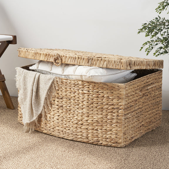 Open woven storage trunk filled with pillows, with its lid raised and a blanket draped over the side