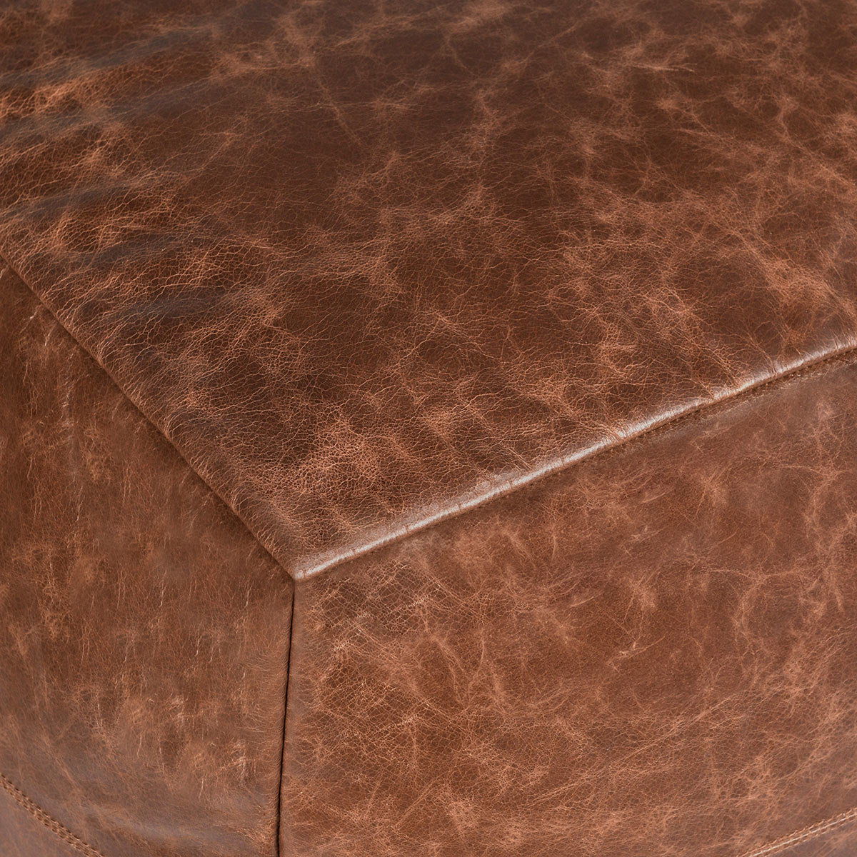 Close-up of chestnut leather pouf with corner seam and stitched edge.