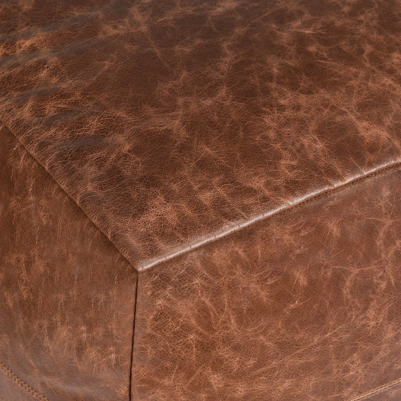 Close-up of chestnut leather pouf with corner seam and stitched edge.