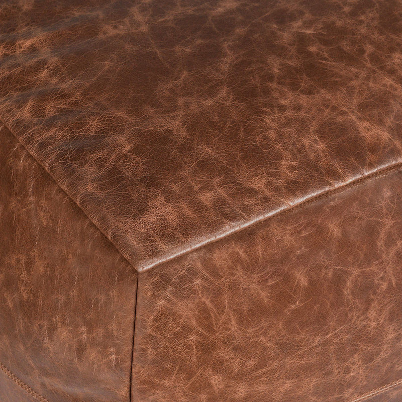 Close-up of chestnut leather pouf with corner seam and stitched edge.