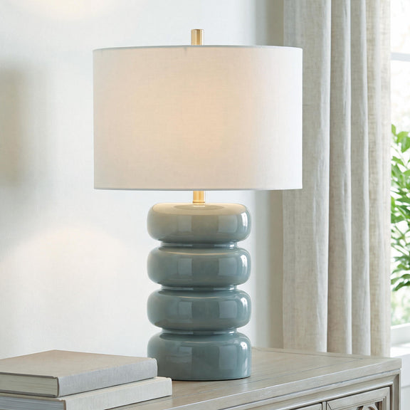 Ceramic table lamp with gray-blue stacked base, brass stem, and white drum shade