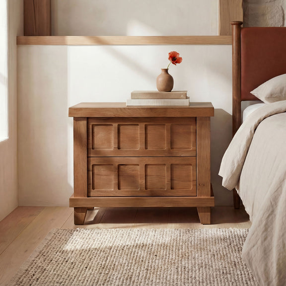 Light wood nightstand with two drawer fronts and tapered legs, beside bed