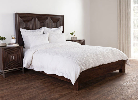 White embroidered duvet and pillows styled on a dark wood bed with decorative headboard