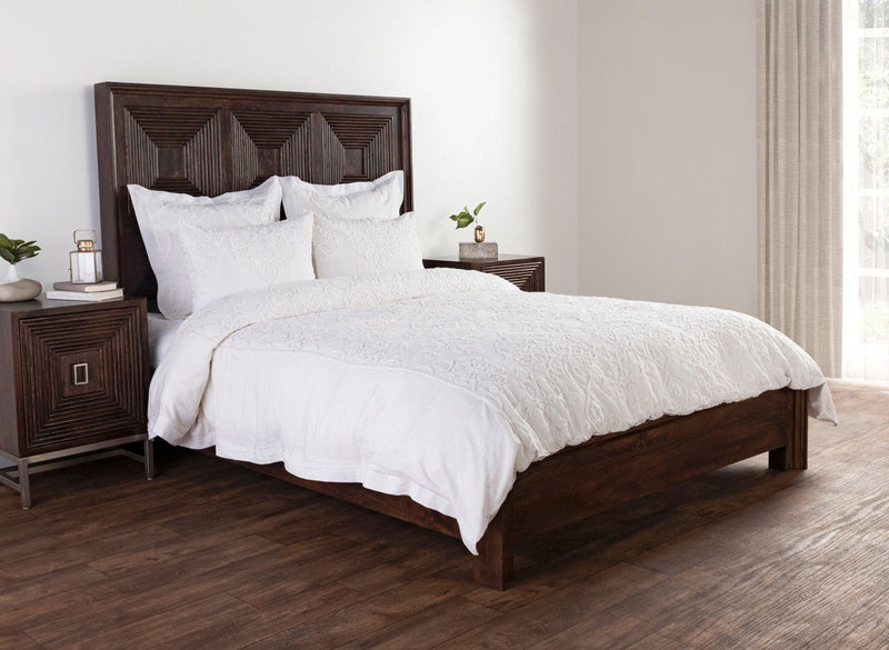 White embroidered duvet and pillows styled on a dark wood bed with decorative headboard