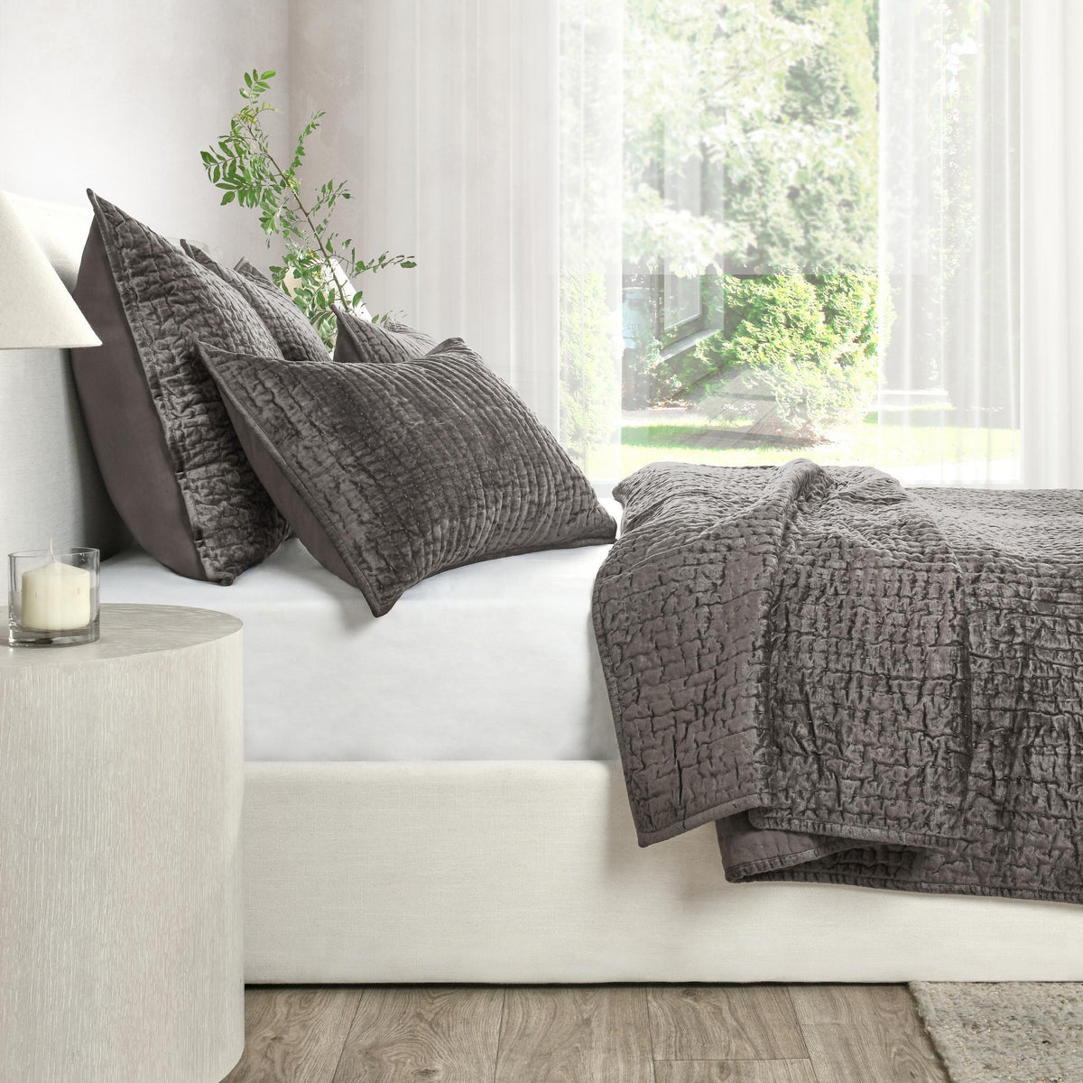 Dark gray velvet quilt set with textured quilt and matching pillow shams on sofa.