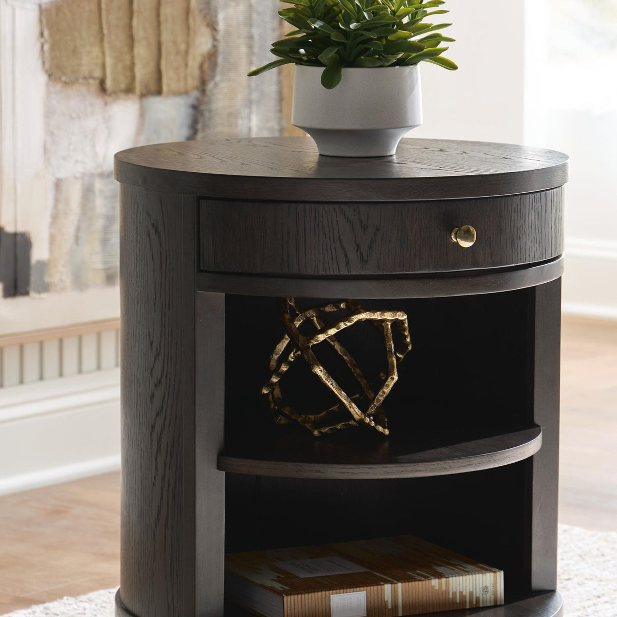 Dark brown round accent table with open middle shelf and drawer front with brass knob