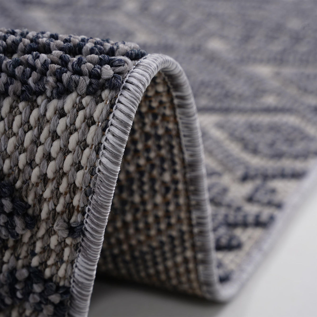 Dark gray rug corner close-up with thick loops and light striped fringe trim.