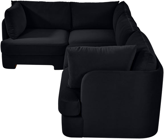 Black velvet sectional sofa with curved armrests and a matching throw pillow