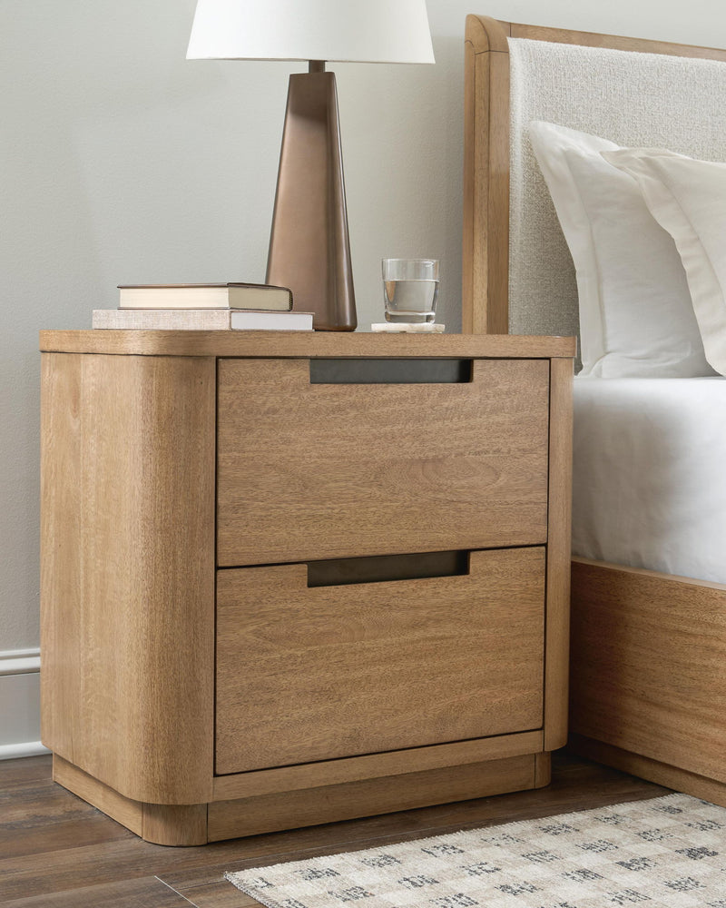 Light brown two-drawer night stand beside bed, featuring black bar pull handles.
