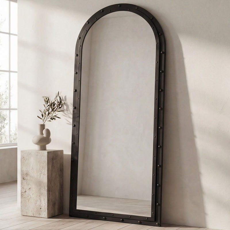 Standing arched floor mirror with dark, studded frame