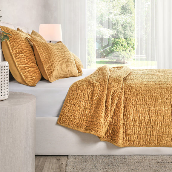 Golden yellow velvet quilt set with textured quilt and coordinating pillows on sofa.