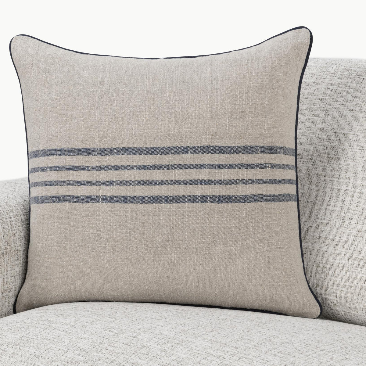 Natural linen pillow with blue stripe band and dark piping, shown on a sofa.