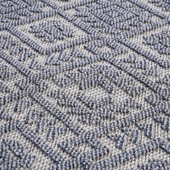 Blue-gray rug close-up with repeating geometric pattern in a textured looped weave.
