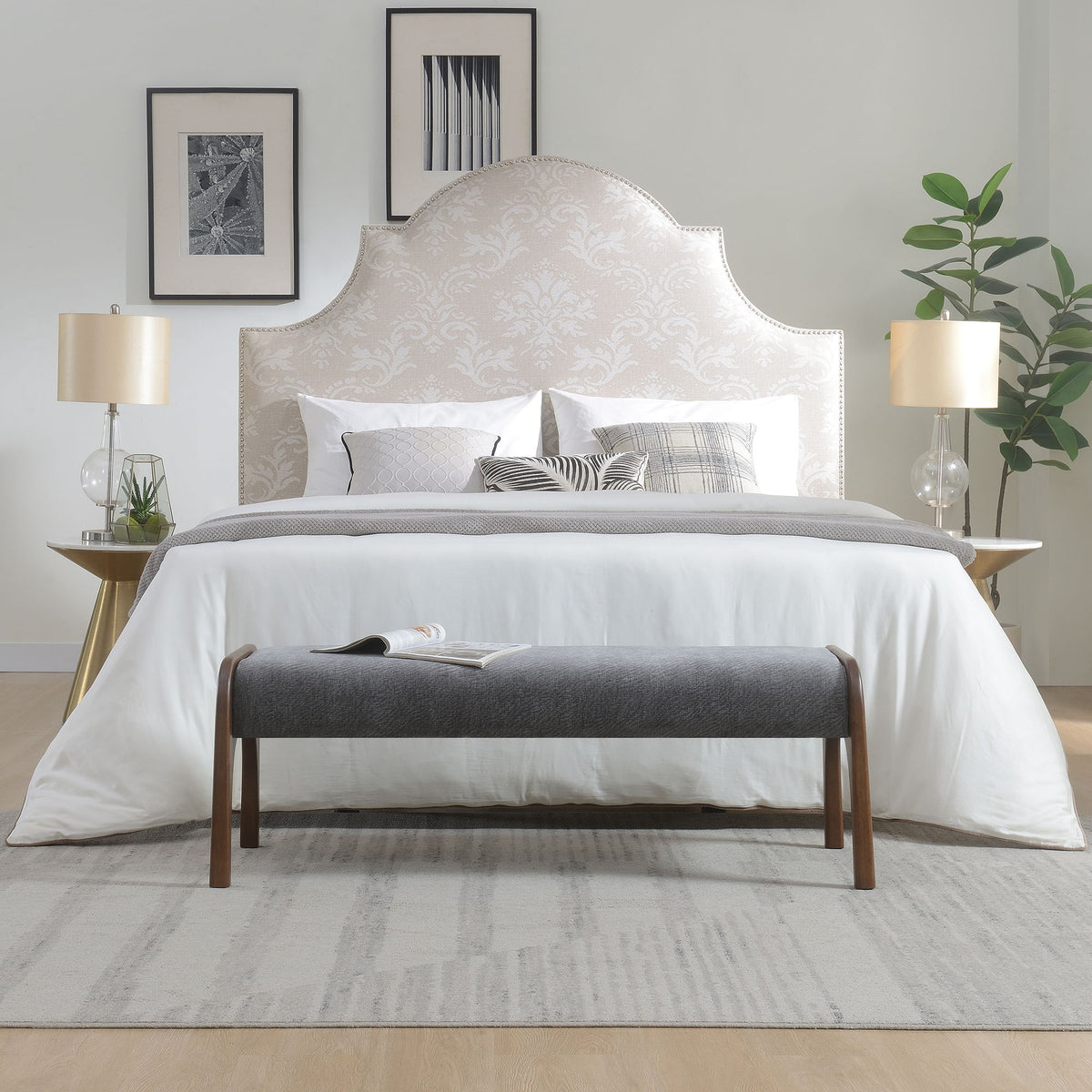 Gray upholstered bench with wooden legs in front of a bedroom bed