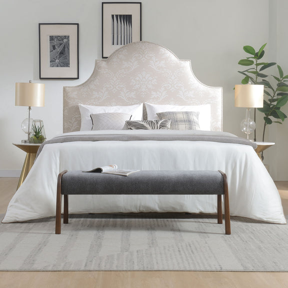 Gray upholstered bench with wooden legs in front of a bedroom bed