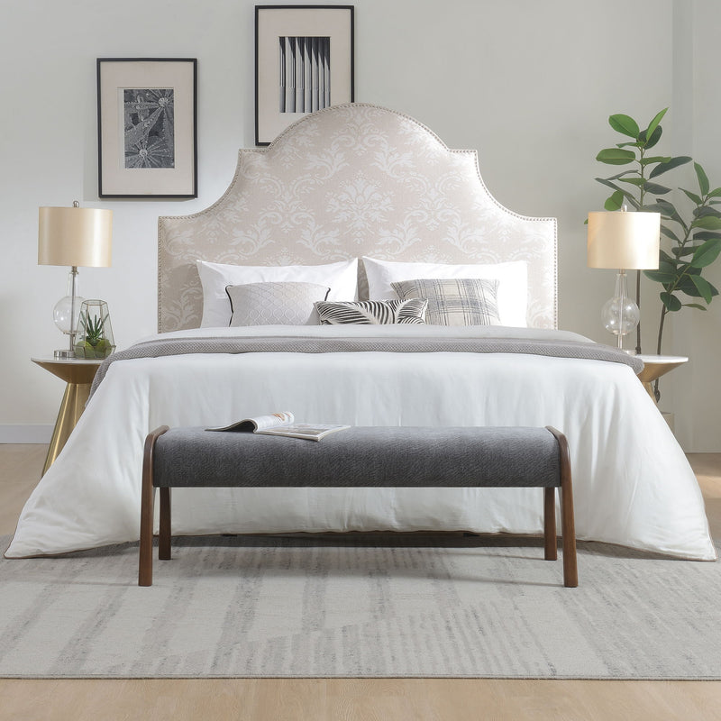Gray upholstered bench with wooden legs in front of a bedroom bed