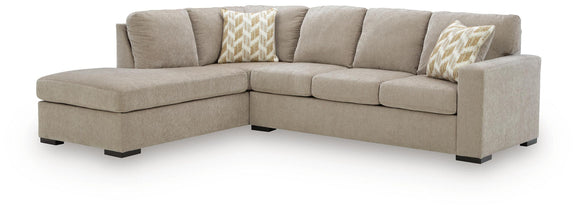 Beige corner chaise sectional sofa with smooth back cushions and two patterned throw pillows.