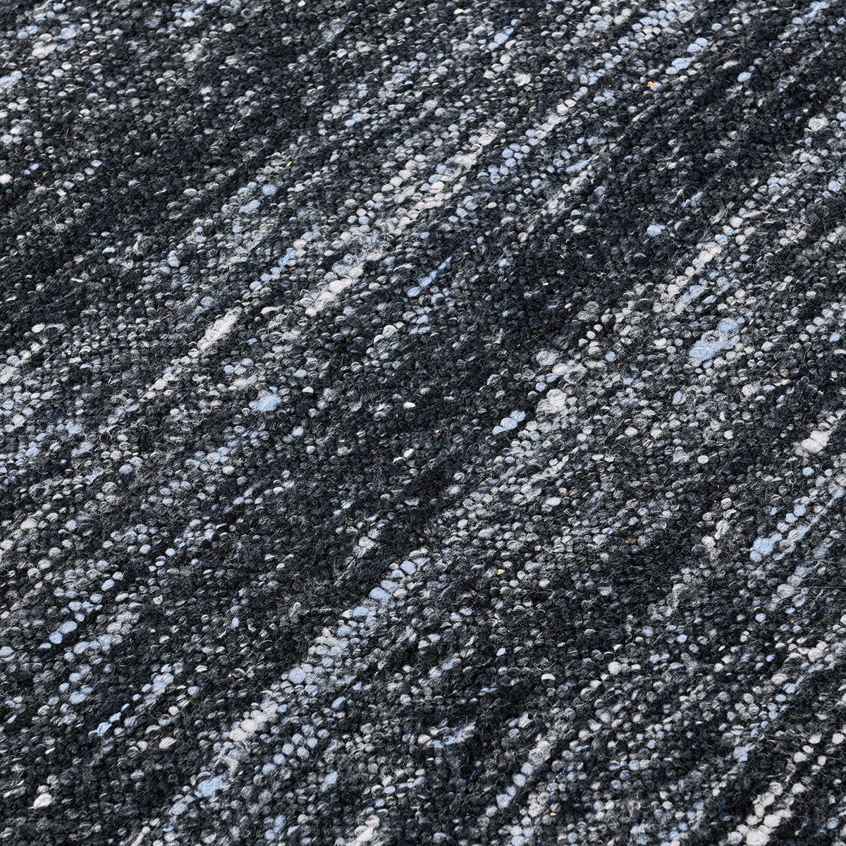 Close-up of dark blue area rug showing speckled texture and woven stripe pattern.