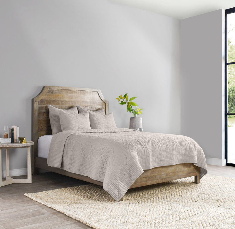Light-colored quilted decorative shams arranged on a bed, featuring subtle texture.
