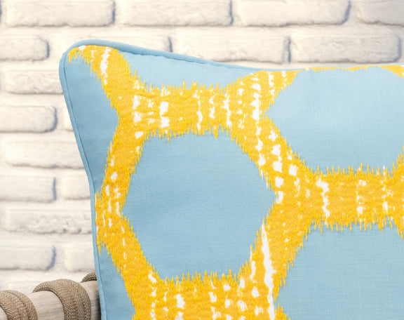 Blue pillow with yellow geometric lattice pattern and textured fringe at the corner