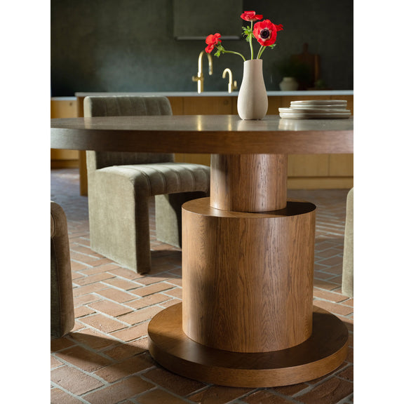 Brown wood dining table shown close up, highlighting its round top and pedestal base