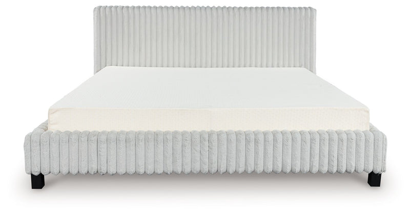 Ivory upholstered bed frame with ribbed headboard and base, white mattress and pillow.