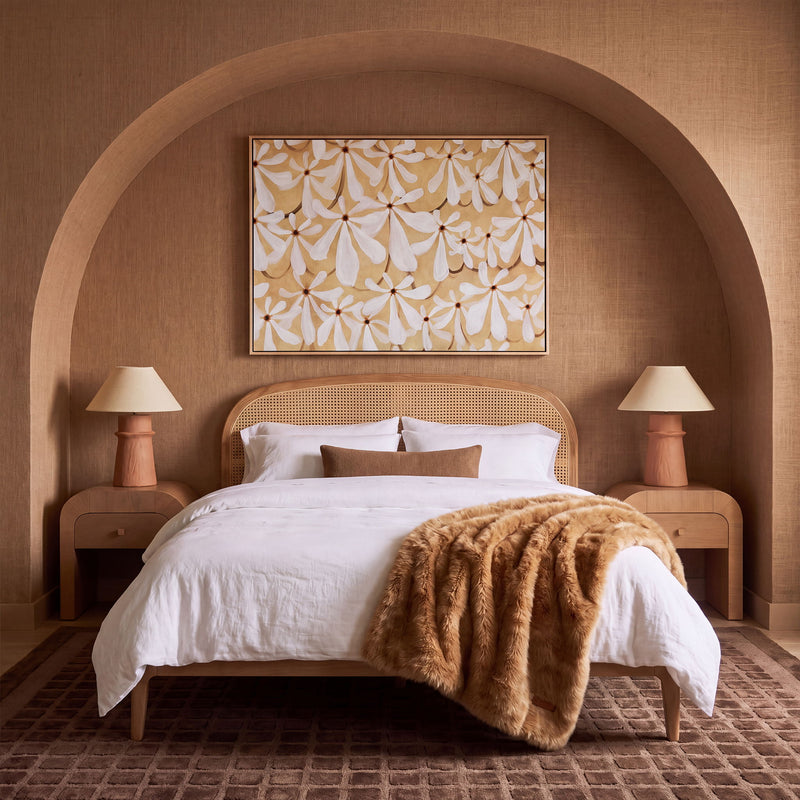 Light brown rattan bed with arched woven headboard and white bedding with brown throw