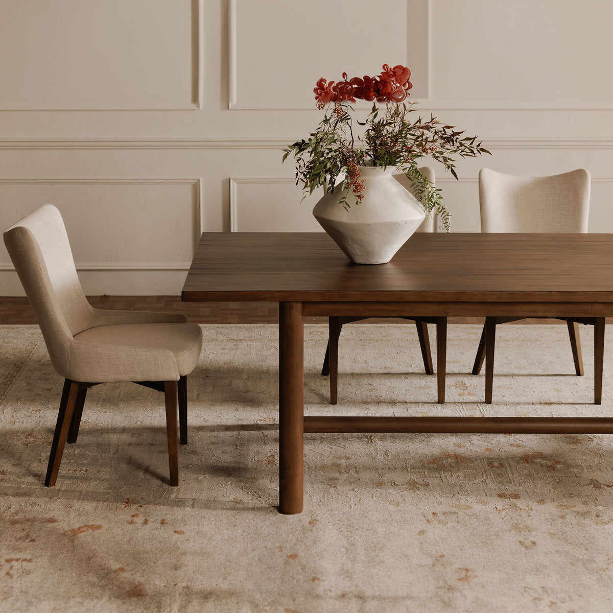 Heather beige upholstered dining chair with dark wood legs, shown beside a dining table