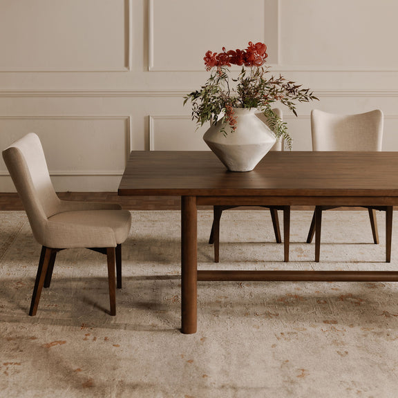 Heather beige upholstered dining chair with dark wood legs, shown beside a dining table