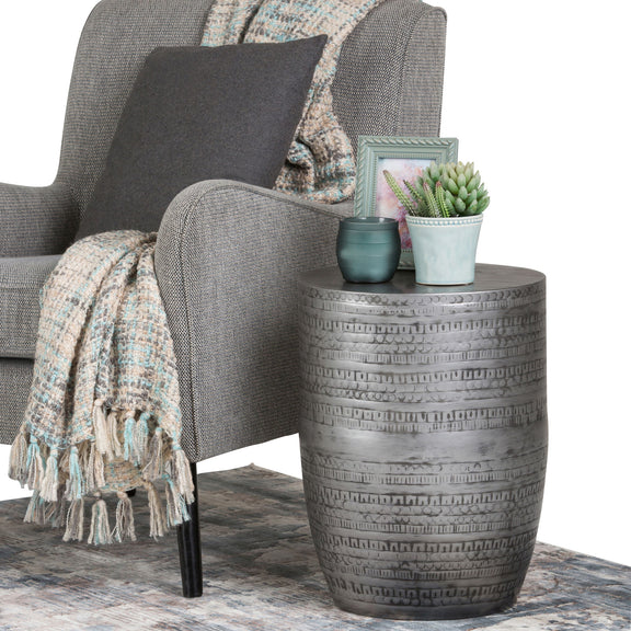 Round metal accent table with embossed bands; top holds small potted plants.