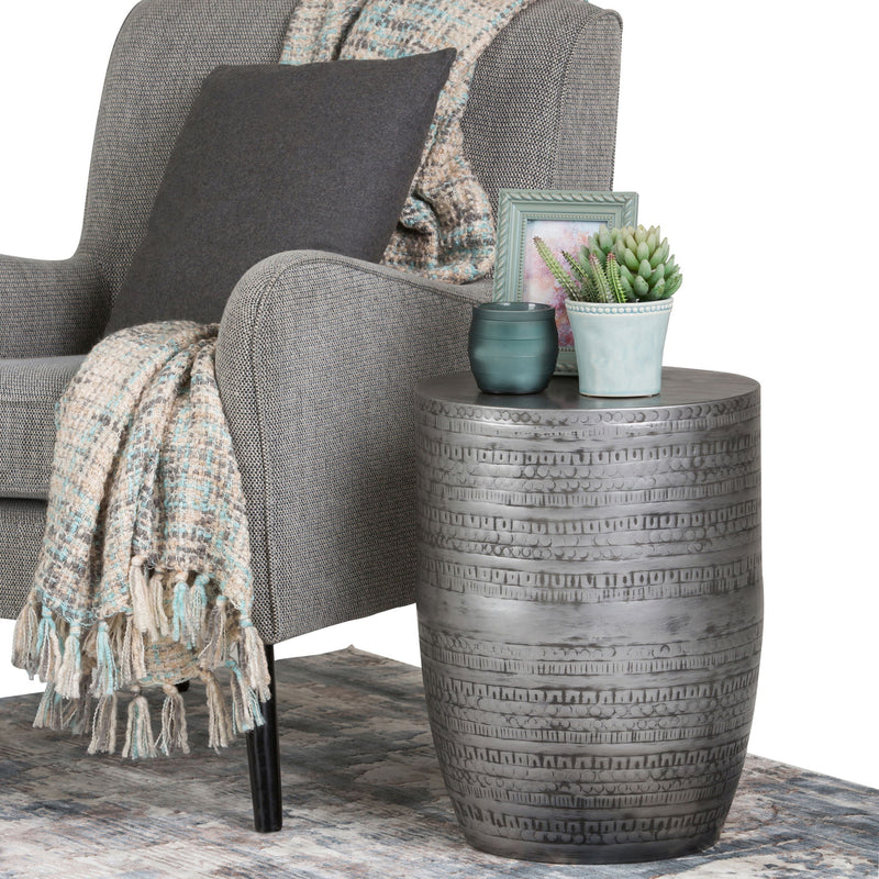 Round metal accent table with embossed bands; top holds small potted plants.
