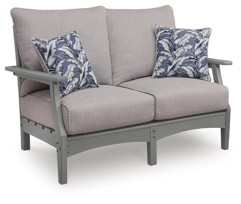 Gray outdoor loveseat with cushioned seat, arms, and two blue leaf-pattern throw pillows